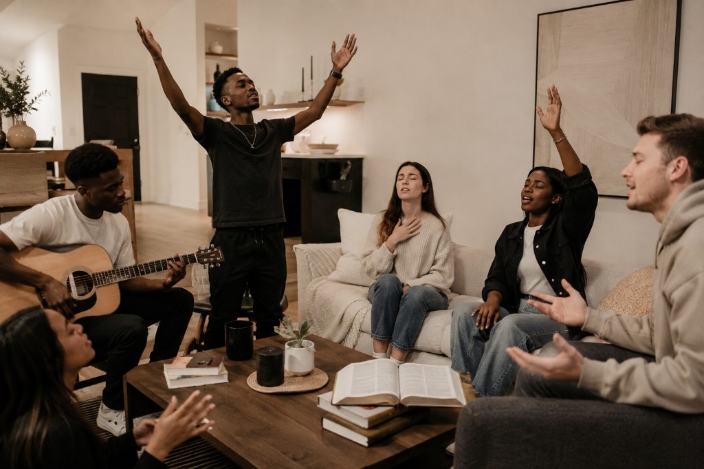 A group worshipping together in a living room with guitar and open Bible.